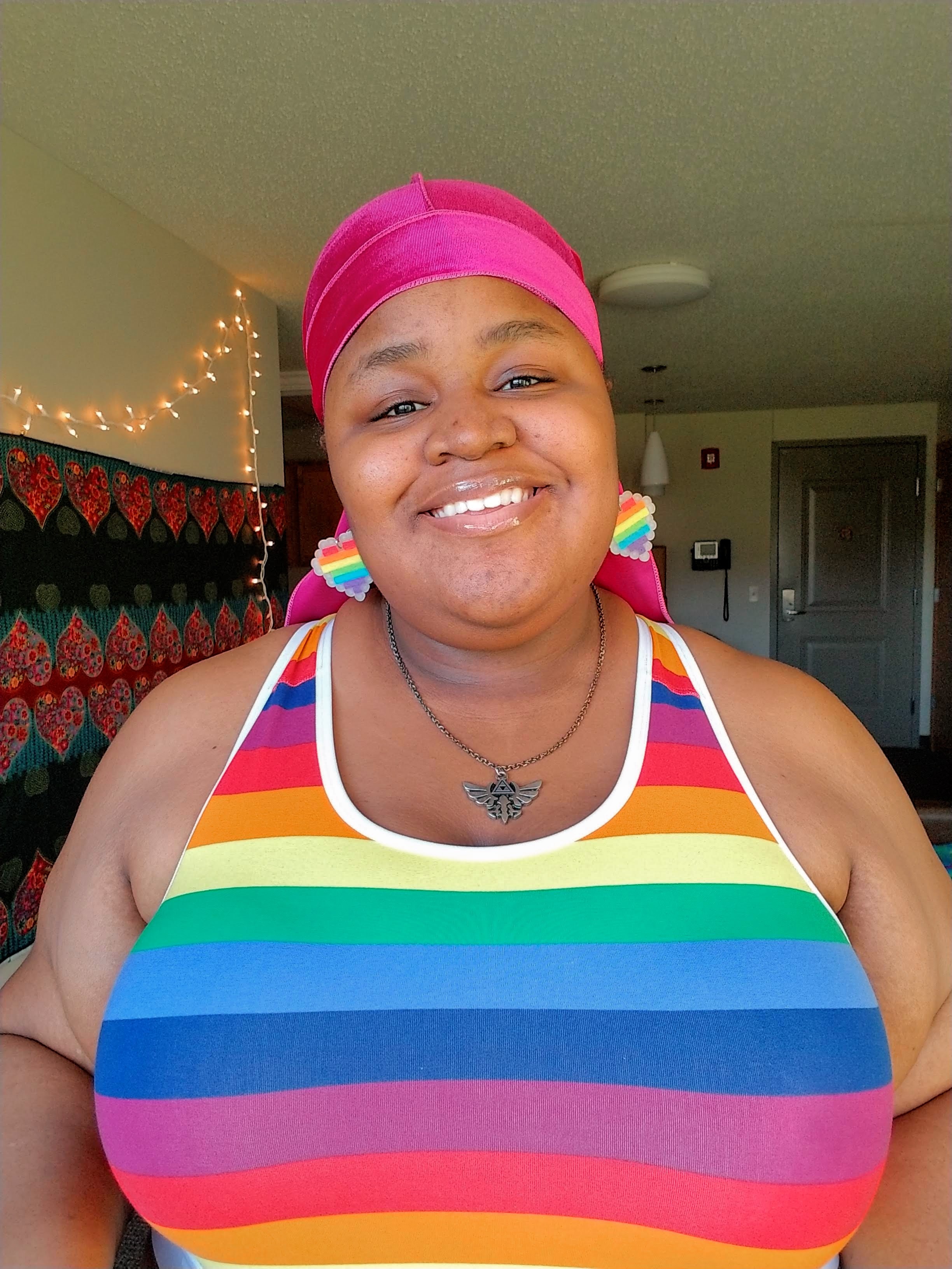 Portrait of Tiana Conyers, smiling wearing a rainbow striped tank top and heart earrings.