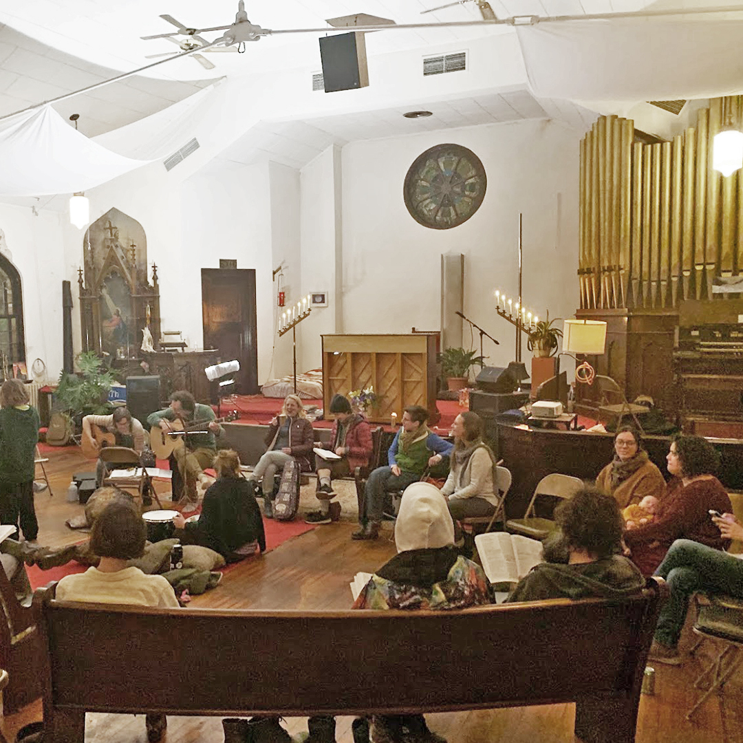 A crowd is gathered in a circle around people playing music Reformed Studio and Assembly Space