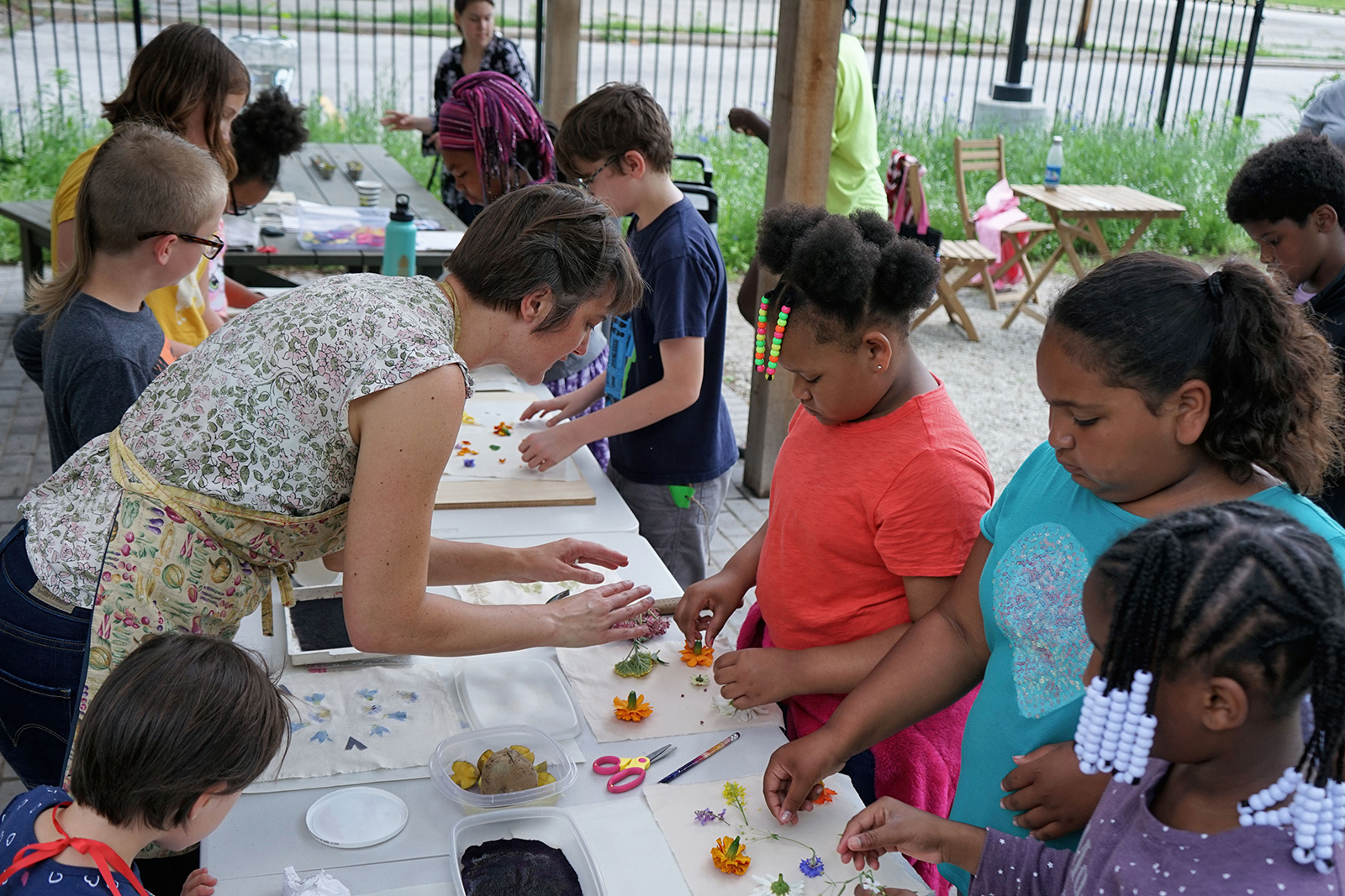 A group of young people standing around a table getting instruction on making prints from flowers from a teaching artist