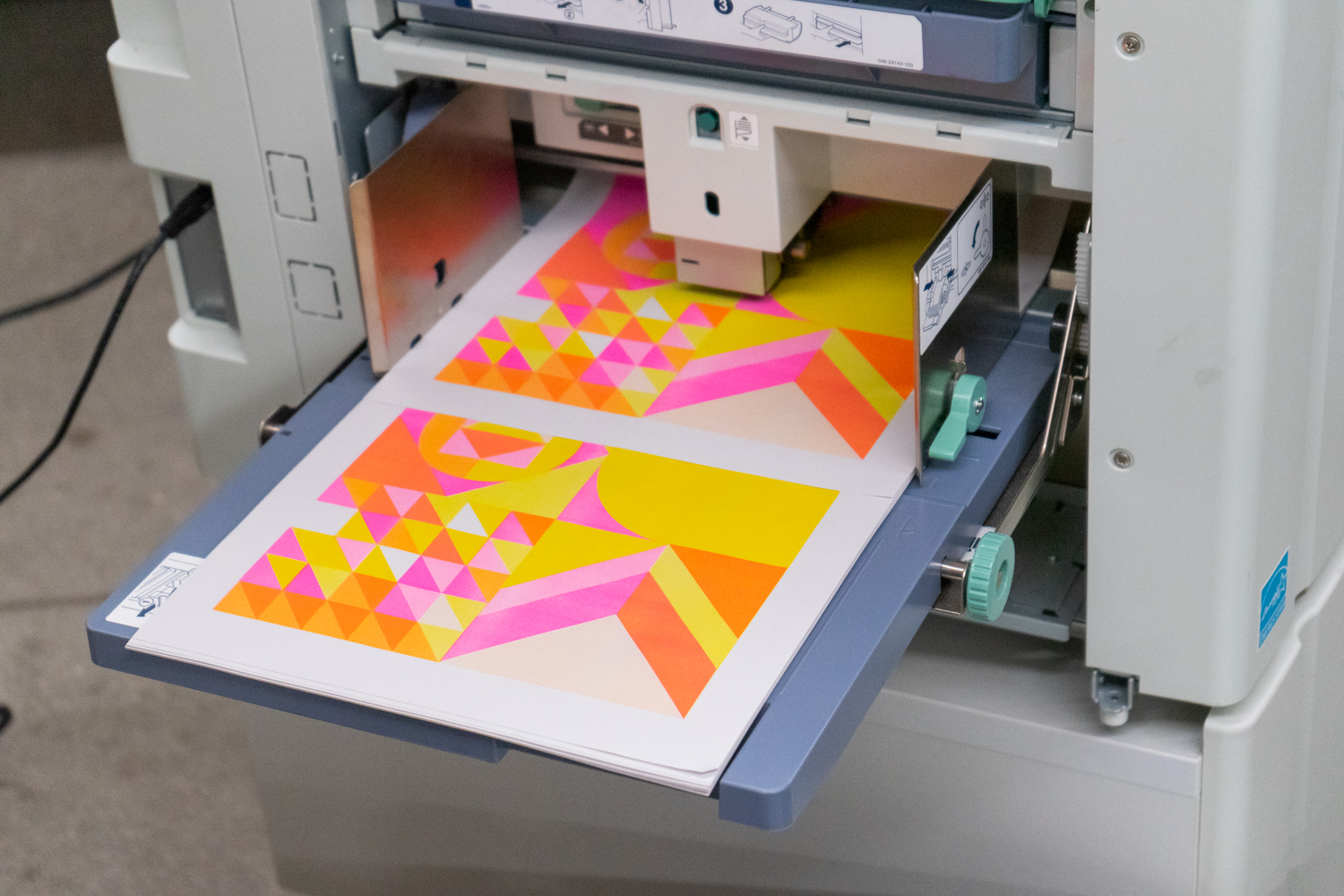 A print with a pink orange and yellow geometric design sits in a risograph tray