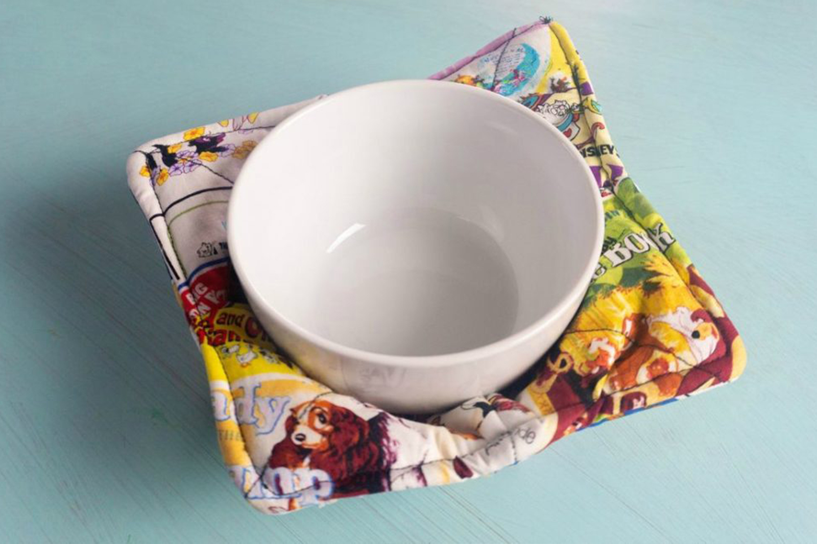 A white bowl sits in a fabric bowl cozy with a colorful pattern