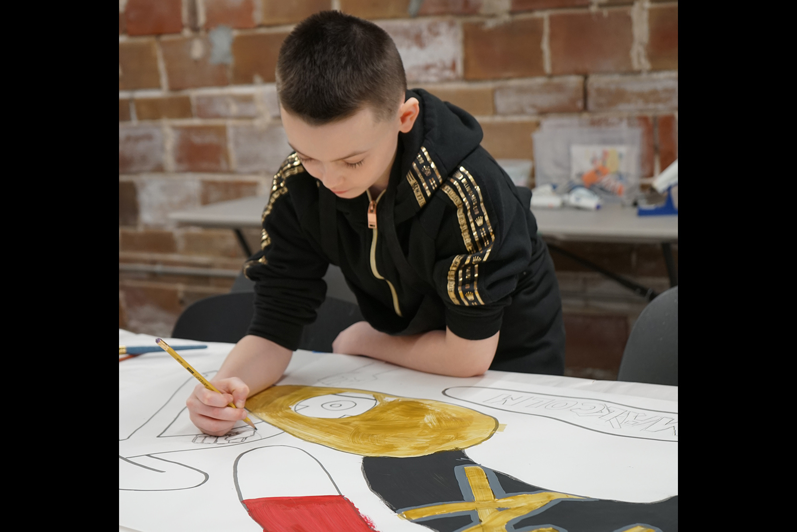 A young boy leans over a large drawing at work with a pencil