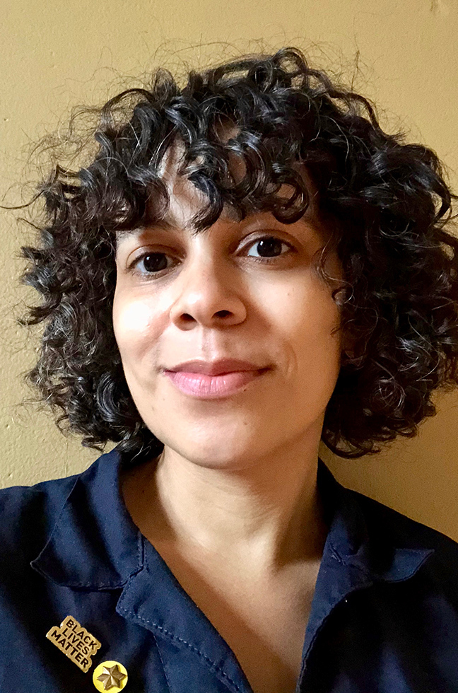 Selfie portrait of Angela Drakeford, the artist, smiling into the camera. The artist wears a dark-blue collared shirt with a gold six-pointed star pin and a gold Black Lives Matter pin.