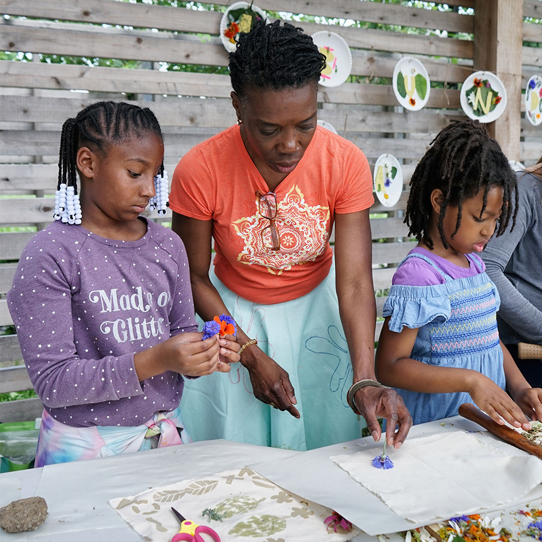 Artist Demetria Geralds works with two young girls creating art with flowers