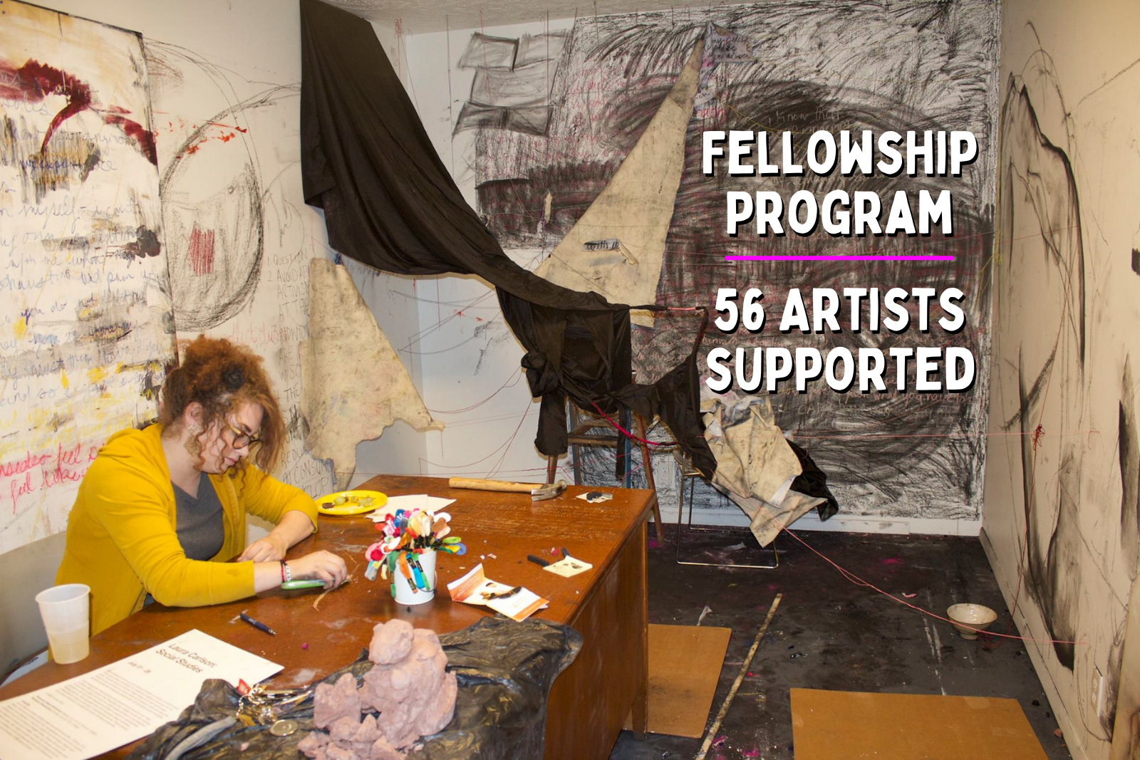 Fellowship Program 56 artists supported photo of artist Bug Carlson at work at a desk and abstract black drawing fills a wall