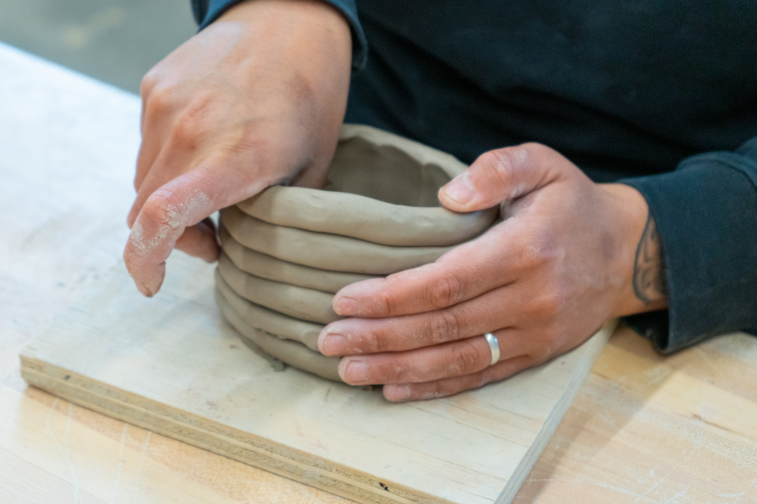 Hands build a coil pot out of clay