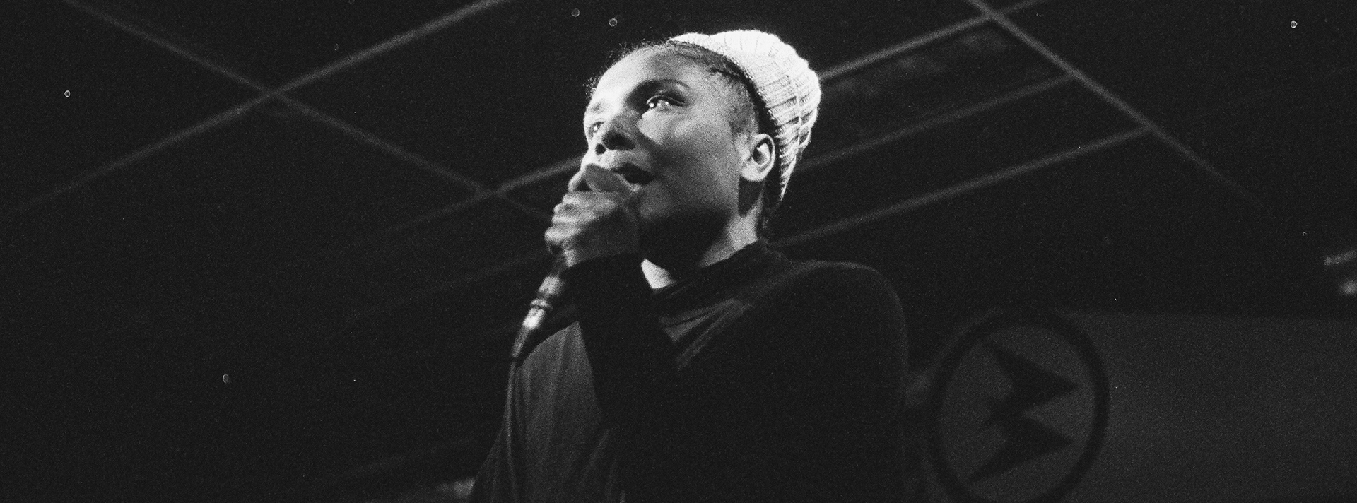 Header A Black and White Portrait of Mary Lawson aka Mesonjixx Holding A Microphone