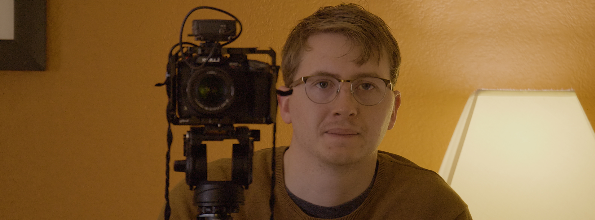Header Image Filmmaker Nick Beaulieu looks in the camera direction while sitting next to a camera on a tripod