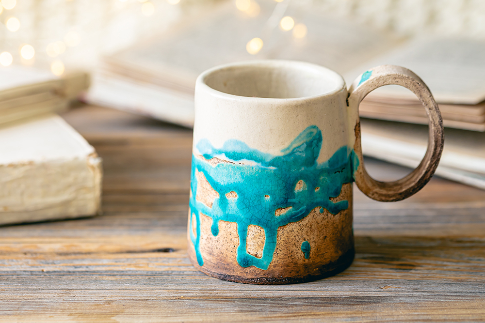 Handmade cup and books close-up on a wooden surface, copy space.