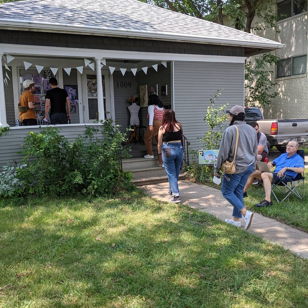 People Gather On A Porch To Look At An Outdoor Art Show