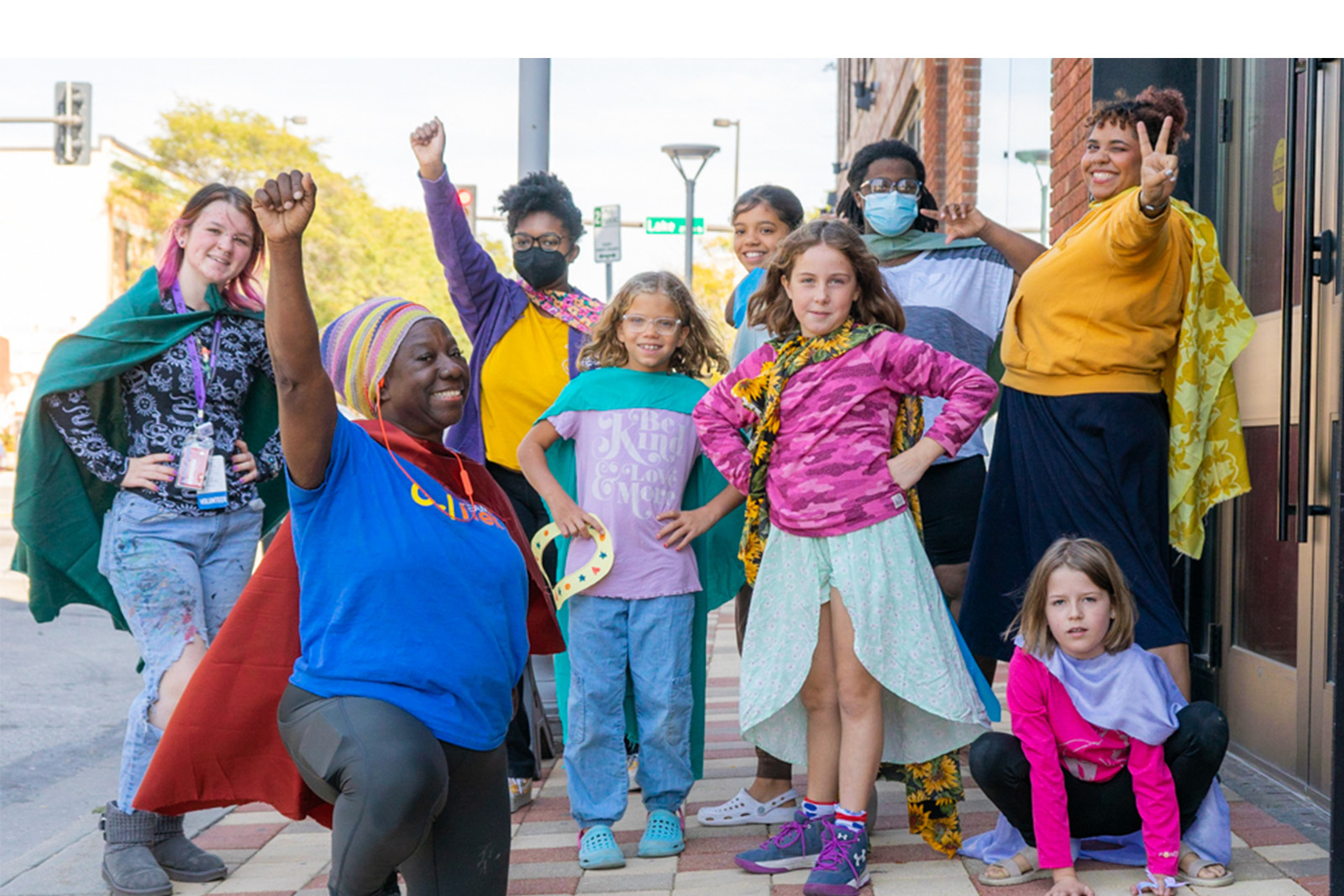 Photo of teaching artists and youth standing outside The Union they are wearing capes and striking super hero poses