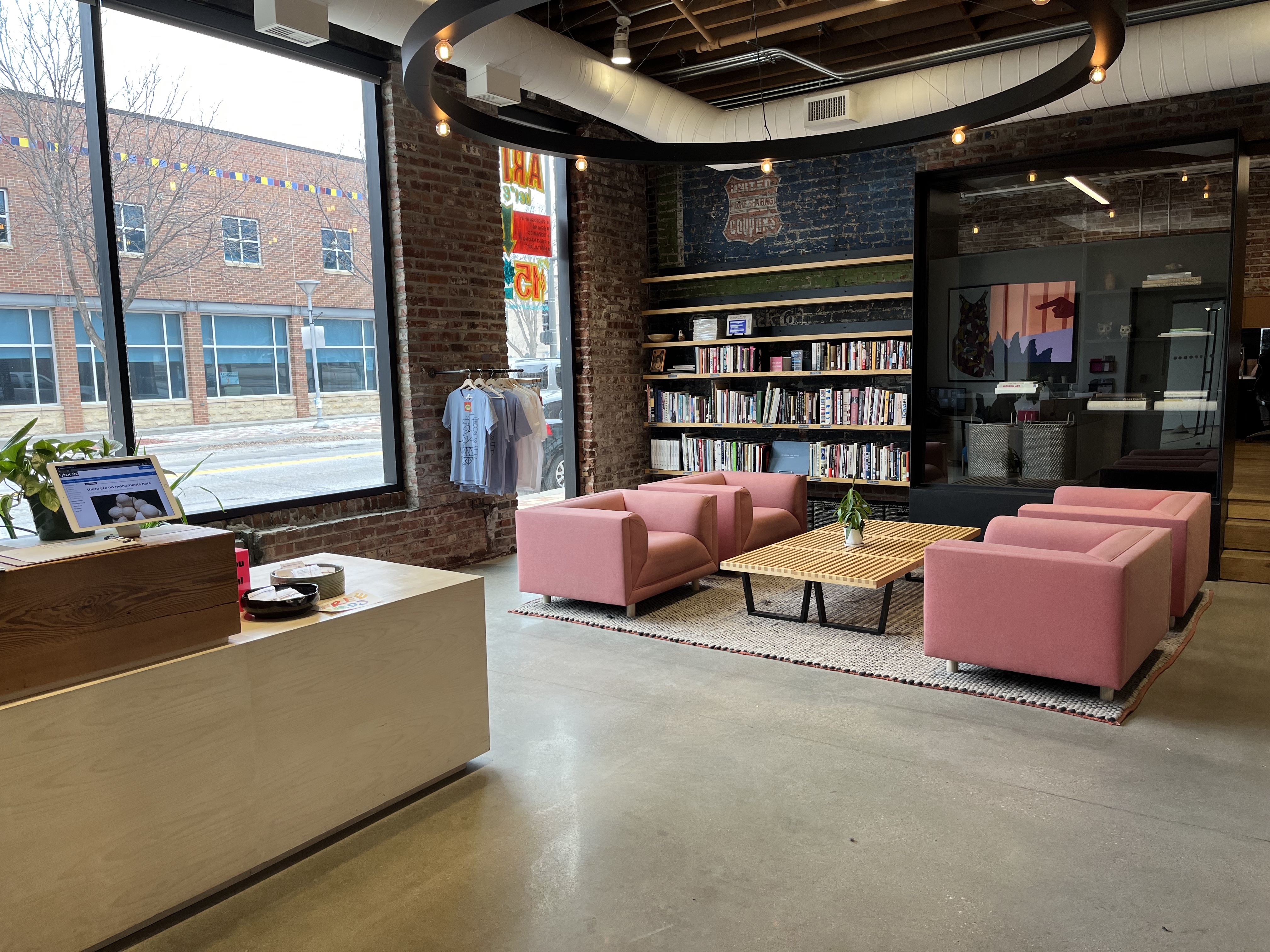 Photo of the reception area at The Union Four pink chairs surround a low table in front of a large bookcase The floor is smooth concrete