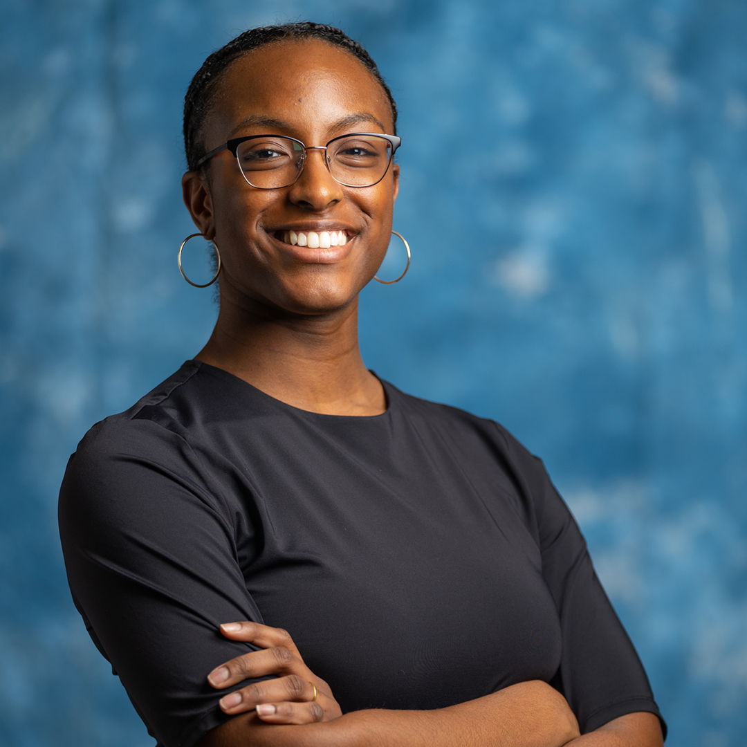 Populus Fund Grantee Jewel Rodgers smiles with arms folded against an abstract blue background