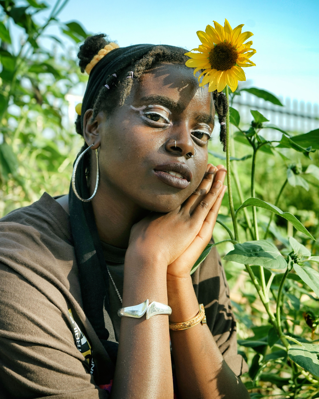 Portrait of Alajia Mc Kizia in a garden her hands near her face sitting next to a sunflower