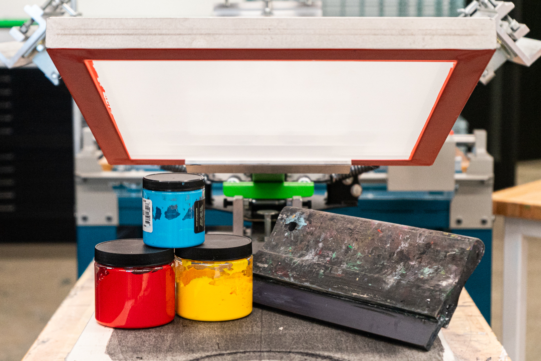 Screenprinting Happenings Ink and a squegee sitting below a screenprinting screen