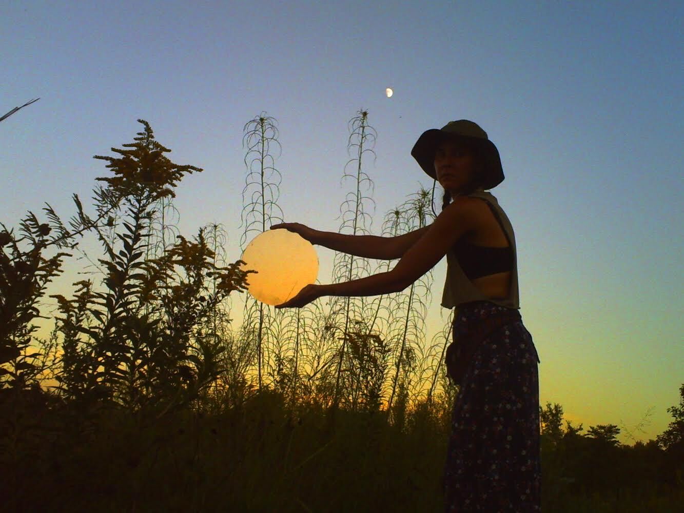 Silhouette of artist Lydia Cheshewalla holding a glowing orb against a sunset