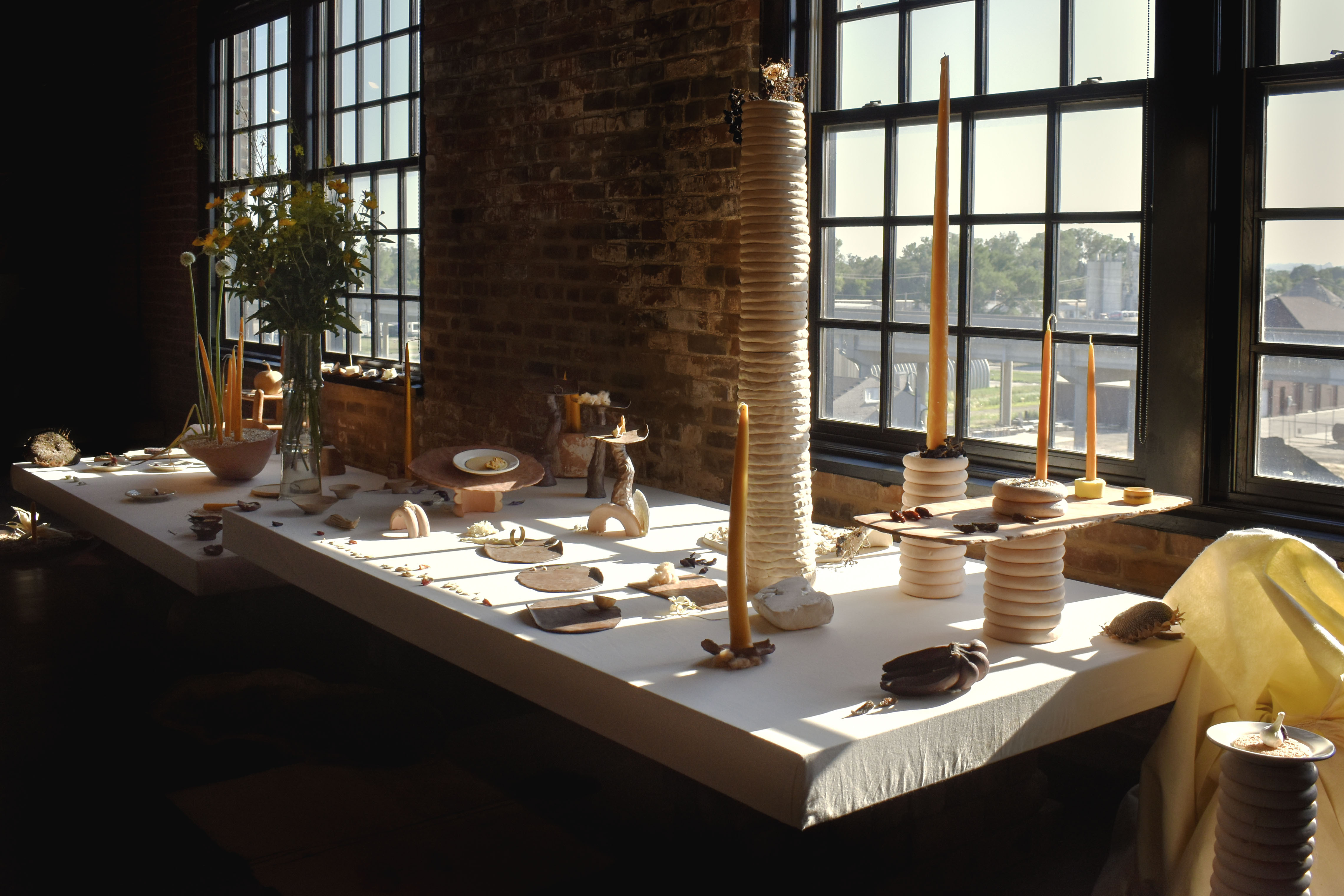 Tall candle sticks and scultural art sit on a table while warm sunlight spills across the scene from a nearby window