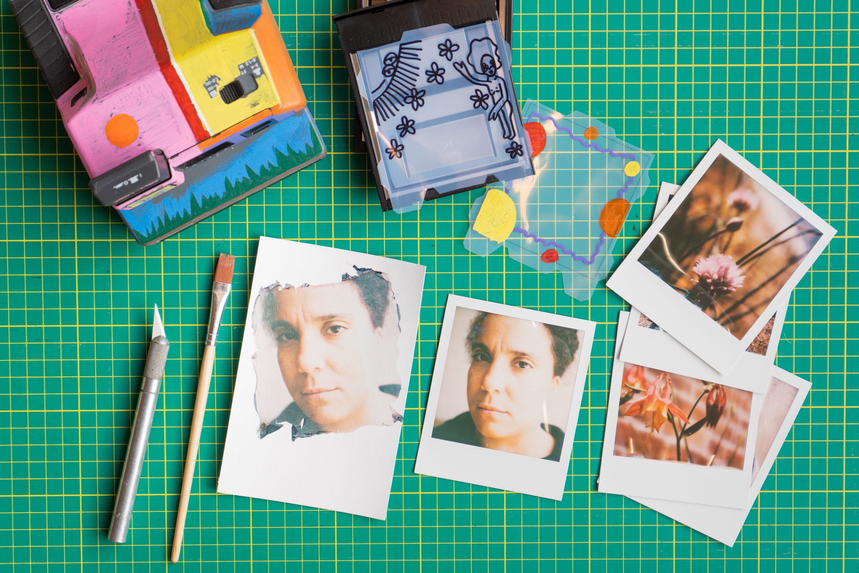 Top down view of polaroids an emulsion lift and a camera on a green cutting mat