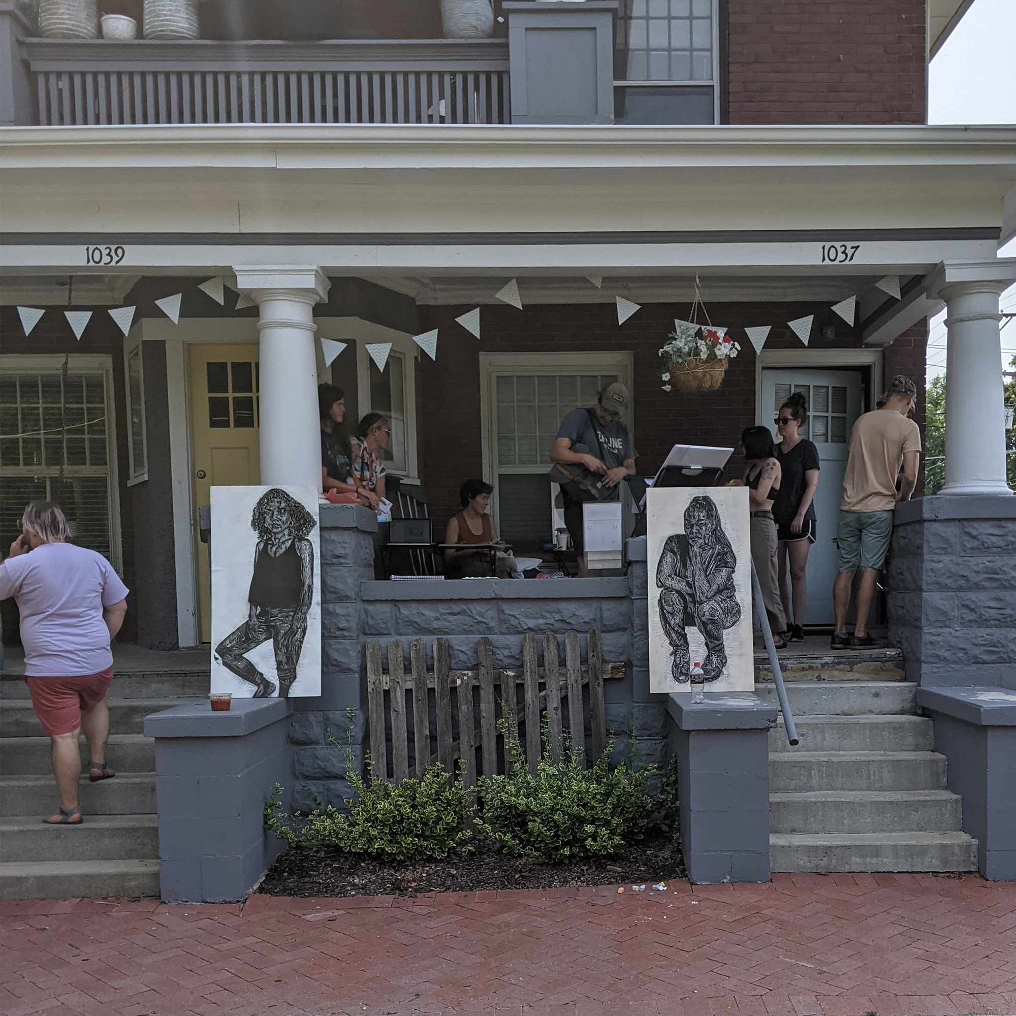 Two Canvases With Illustrations Sit On Two Neighboring Porches While People Gather On The Right Porch Crop