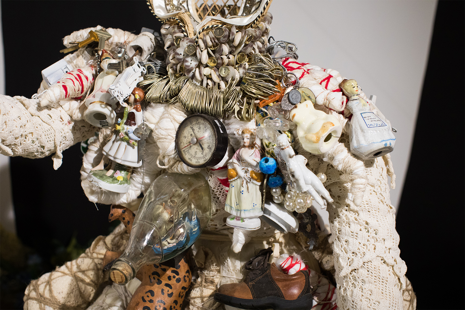 Vanessa German - detail of figure in white, adorned with several found object antique pieces. Many are Victorian era porcelain figures of caucasian "upper class" women. There is also a necklace of soda can tops, an old clock, and a baby's shoe.
