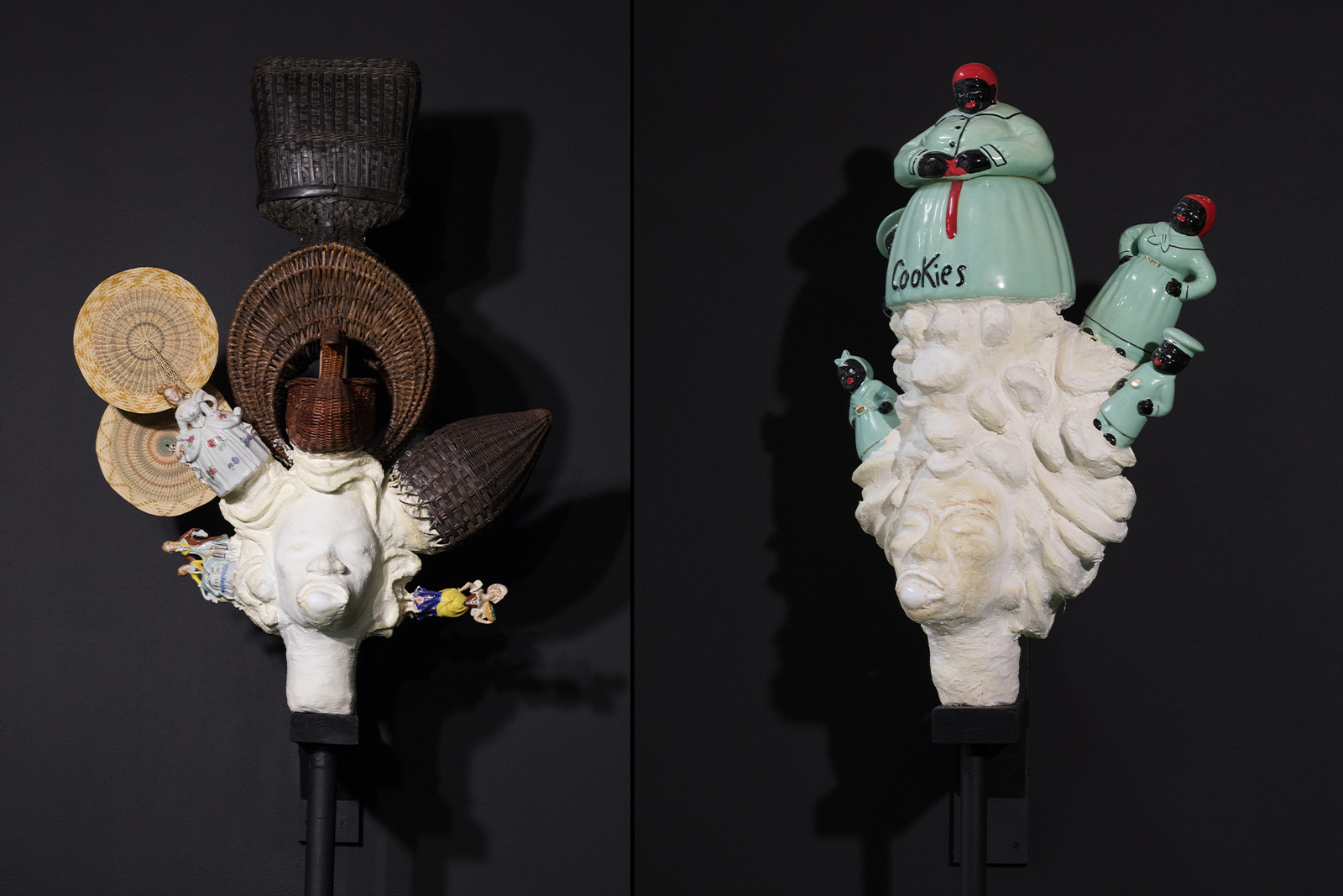 Vanessa German - Two white sculpted heads against a black wall in the exhibit antechamber. The heads, made with large shells for mouths, also include antique ceramic figures.