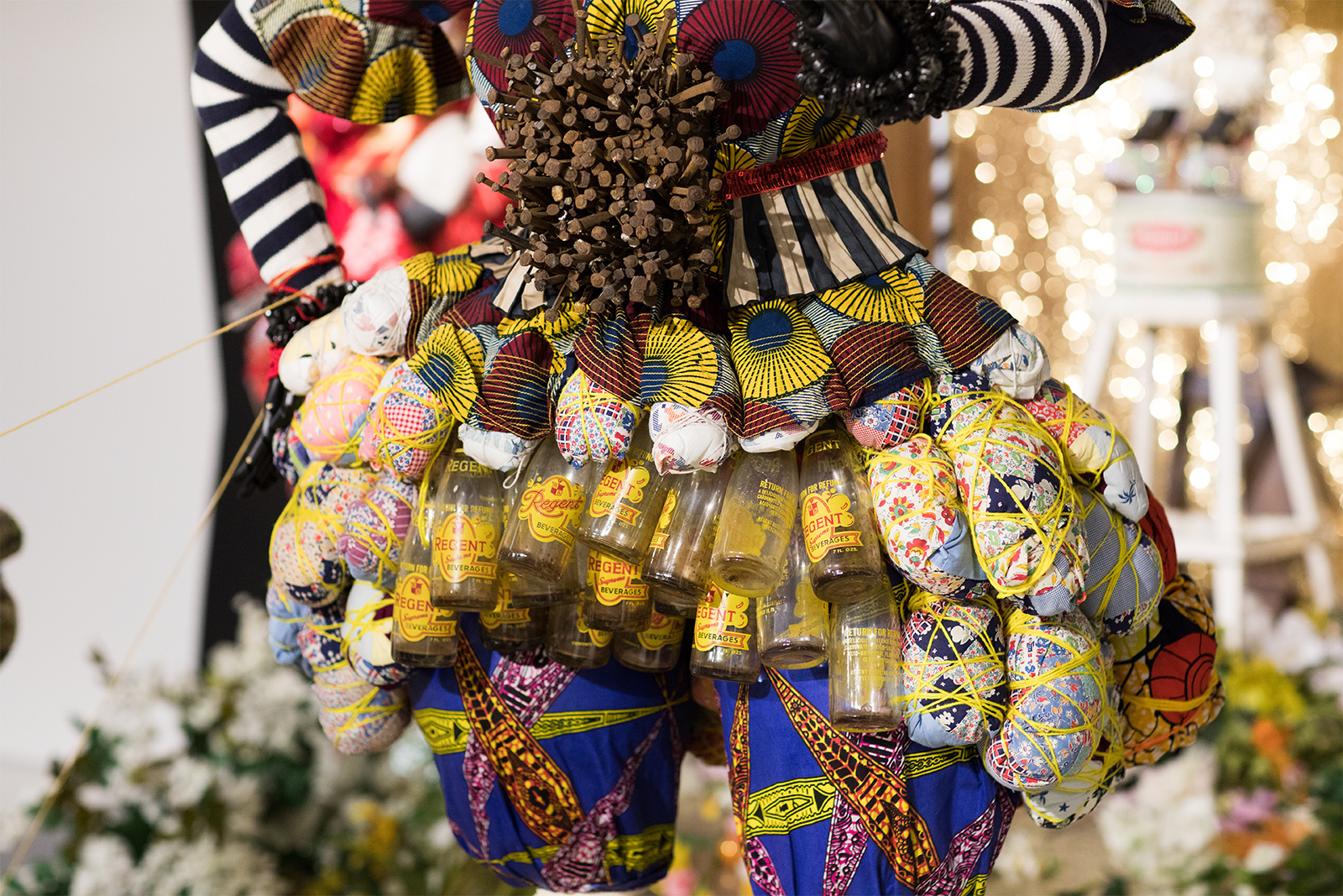 Vanessa German - Detail of assembled figure, wearing a skirt made of bottles, brightly colored fabrics, and a torso full of long, rusted nails.