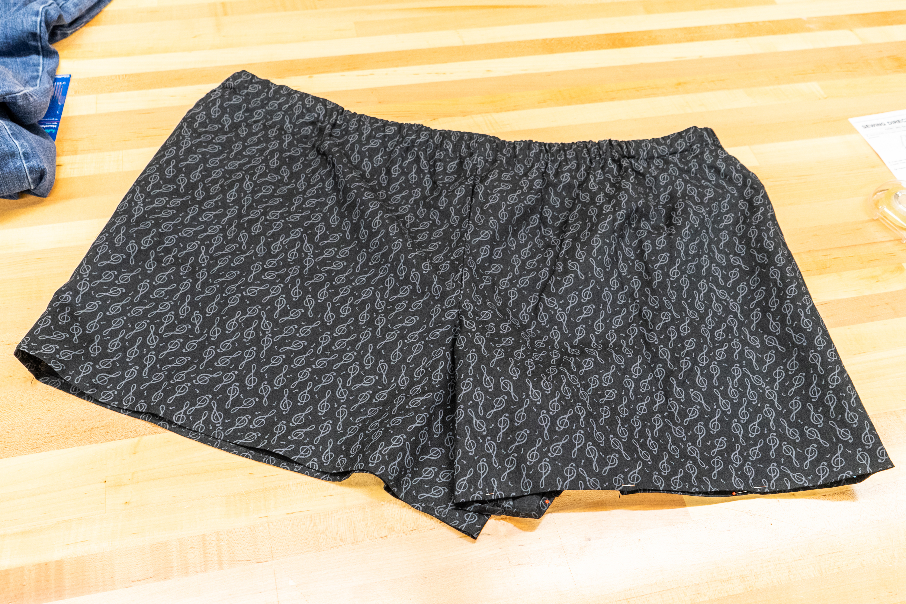 Black shorts with a musical note pattern lie on a wood tabletop