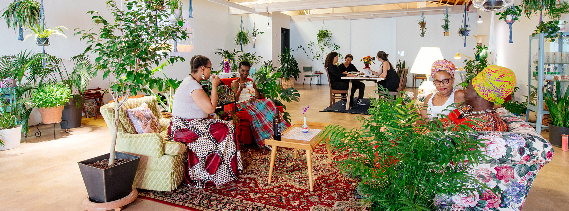 Community members relax in the Wanda D Ewing gallery during the 2019 exhibition 22 Homecoming 22 The space is full of plants rugs and plush furniture