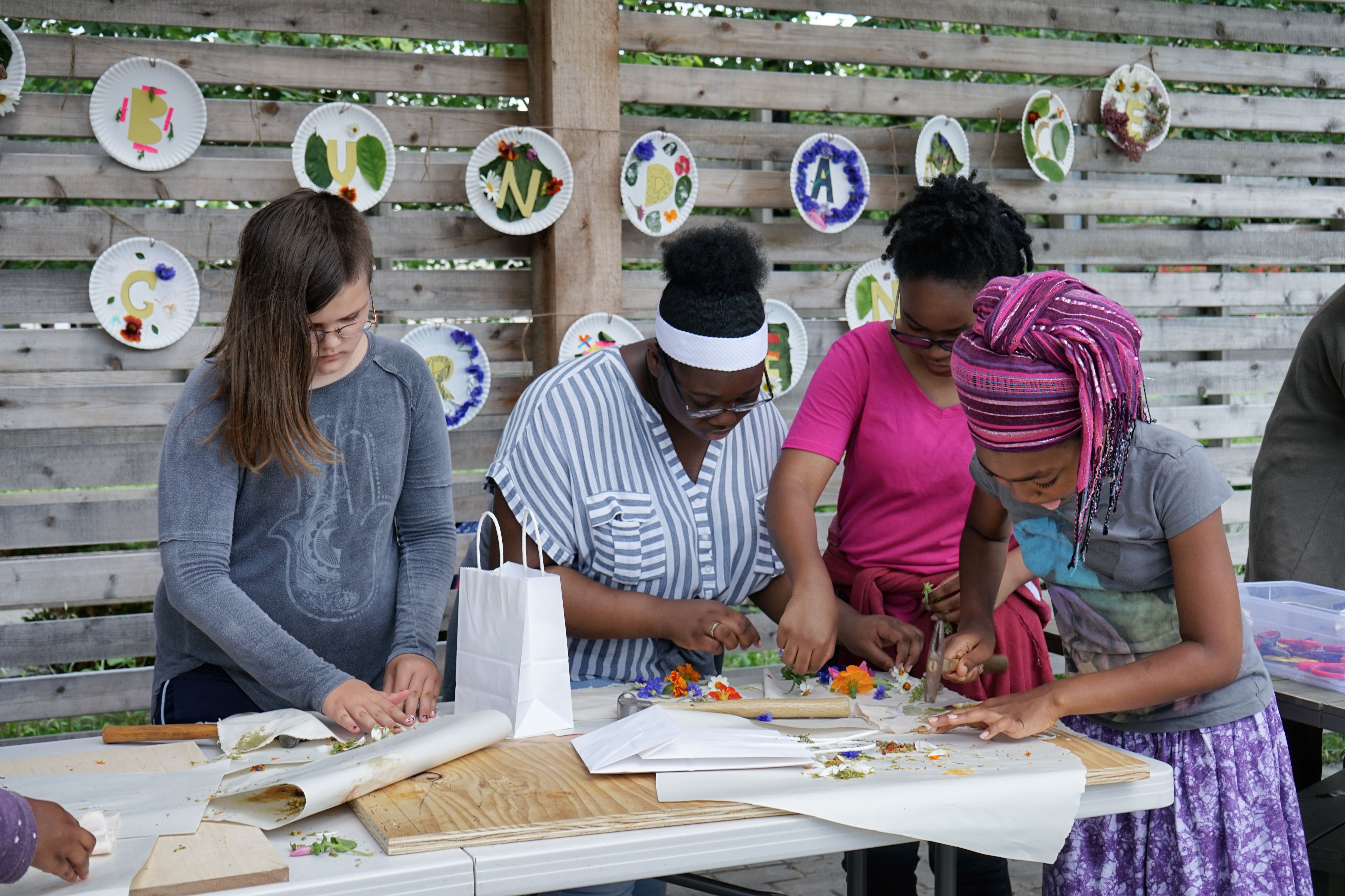 Four young artists create art with flowers around a table outdoors